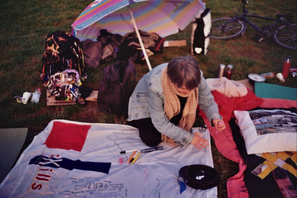 A person is bent over drawing something on a blanket in a park.